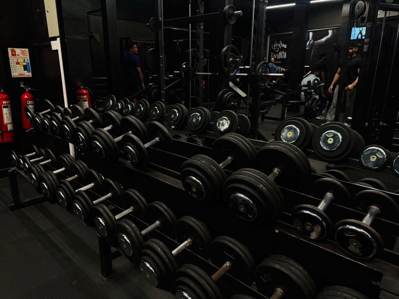 Rows of dumbbells and loaded barbells along the mirrored wall